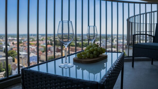 Un balcón con una mesa de vidrio, dos copas de vino y una bandeja de madera con uvas.