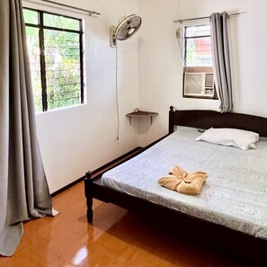 Relax in this serene bedroom with a comfortable bed, a wall-mounted fan, and a view of lush greenery outside.