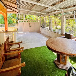 Relax in this serene outdoor patio with a wooden table and bench, surrounded by lush trees.