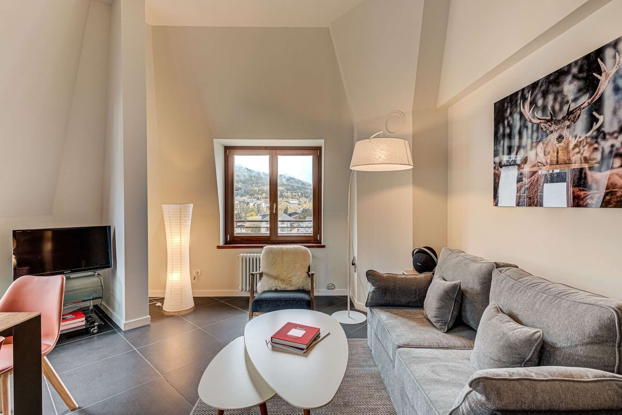 Ett modernt vardagsrum med en soffa, en tv, en lampa och utsikt över ett berg genom ett fönster.
