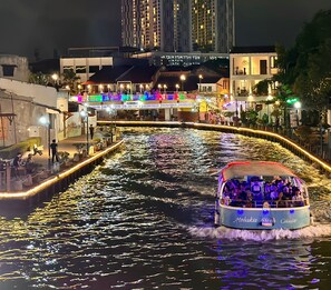 A river cruise boat with passengers, a brightly lit bridge, and buildings in the background. - Wayfarer Guest House Malacca (Malacca City)