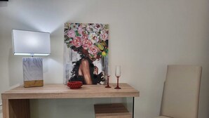 A room with a wooden desk, a painting, a lamp, a red bowl, two wine glasses, and a chair. - Atena apartments 1 Agrigento center: your retreat in Agrigento (Agrigento)