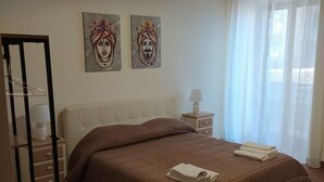 A bedroom with a bed, a nightstand, a lamp, and two wall-mounted paintings. - Atena apartments 1 Agrigento center: your retreat in Agrigento (Agrigento)