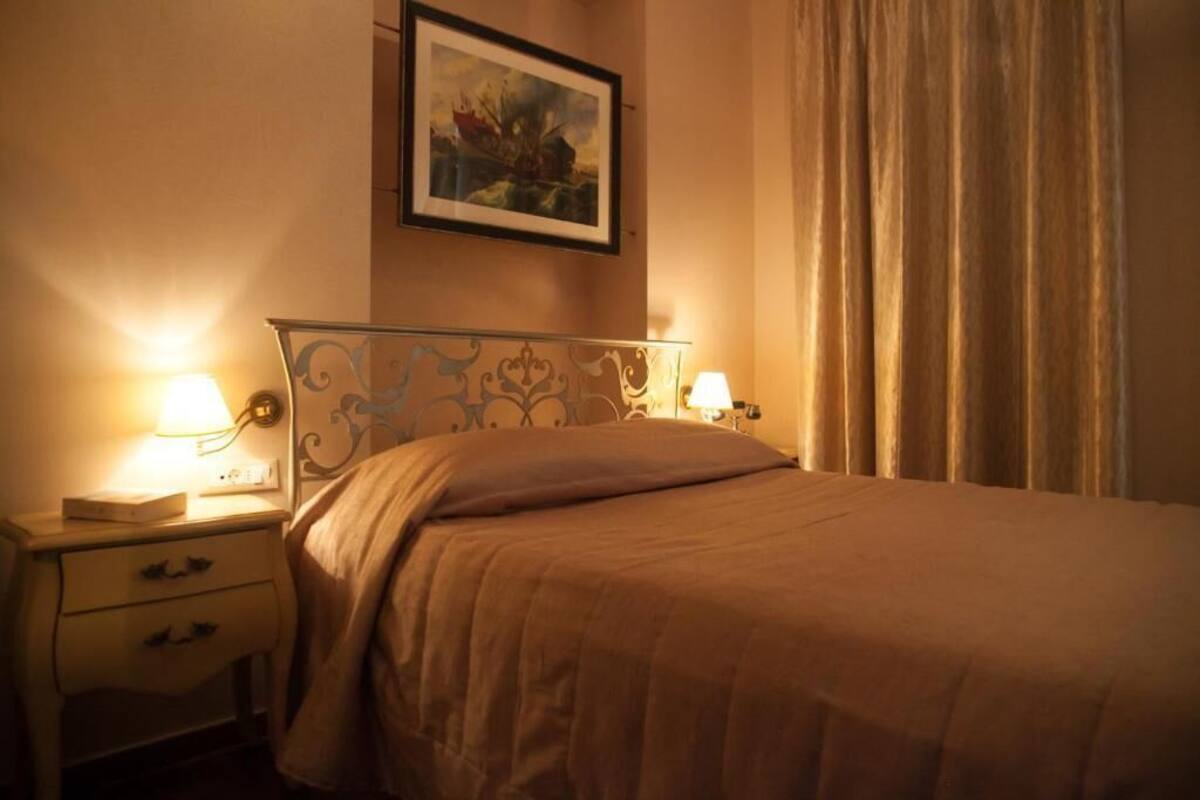 Un llit ben arreglat amb un capçal, dues làmpades de nit, una tauleta de nit amb calaixos i un quadre encapçalat a la paret.
