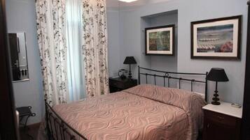 A bedroom with a bed, two bedside tables, a mirror, and two framed pictures on the wall.