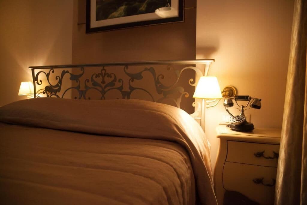 Habitación de hotel con cama, dos lámparas de noche, una mesita de noche con teléfono y un cuadro en la pared.