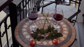 Un balcon avec une table sur laquelle sont posés deux verres à vin et des roses, donnant sur une étendue d’eau et un bâtiment situé au loin.