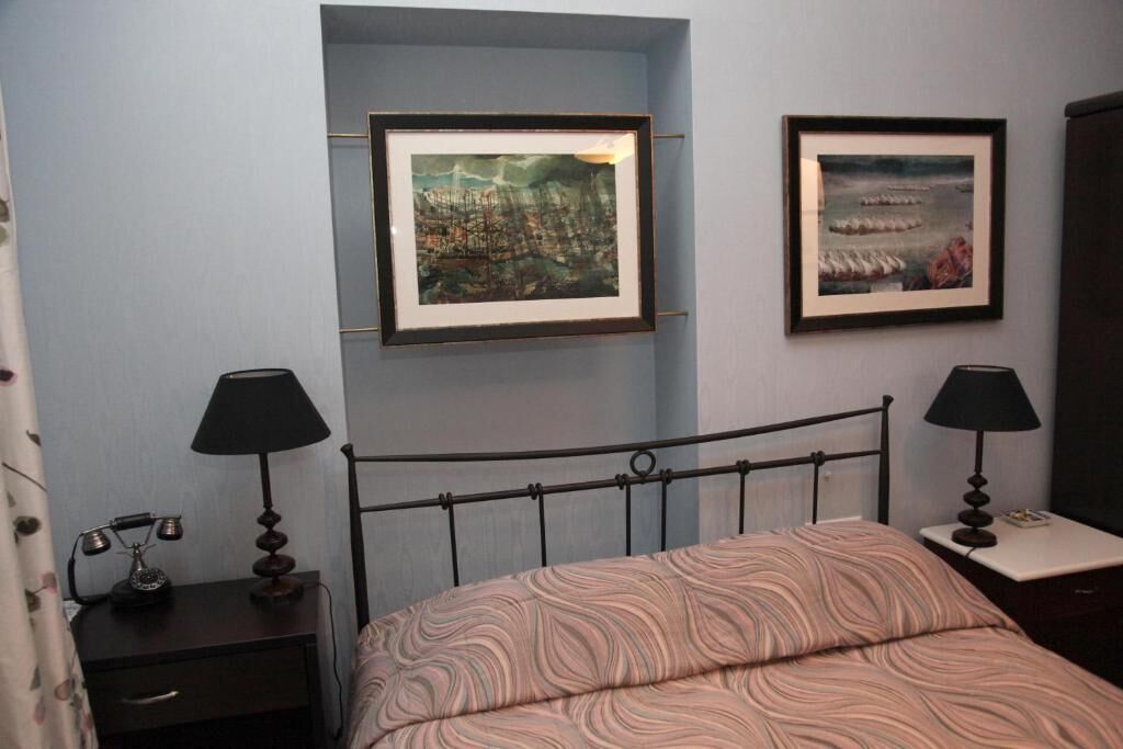 A bedroom with a bed, two bedside tables with lamps, a nightstand, and two framed pictures on the wall.