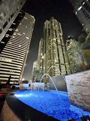 Vista noturna de uma paisagem urbana com edifícios altos e uma fonte.