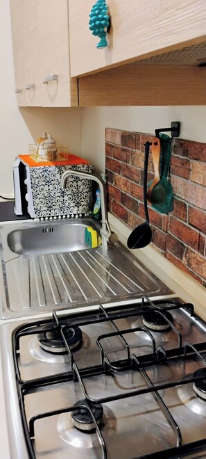 A kitchen with a gas stove, a sink, and a brick backsplash. - Atena apartments 2 Agrigento center (Agrigento)