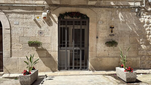Fachada de edificio con un amplio acceso en arco, una cámara de seguridad y un letrero que indica una suite.
