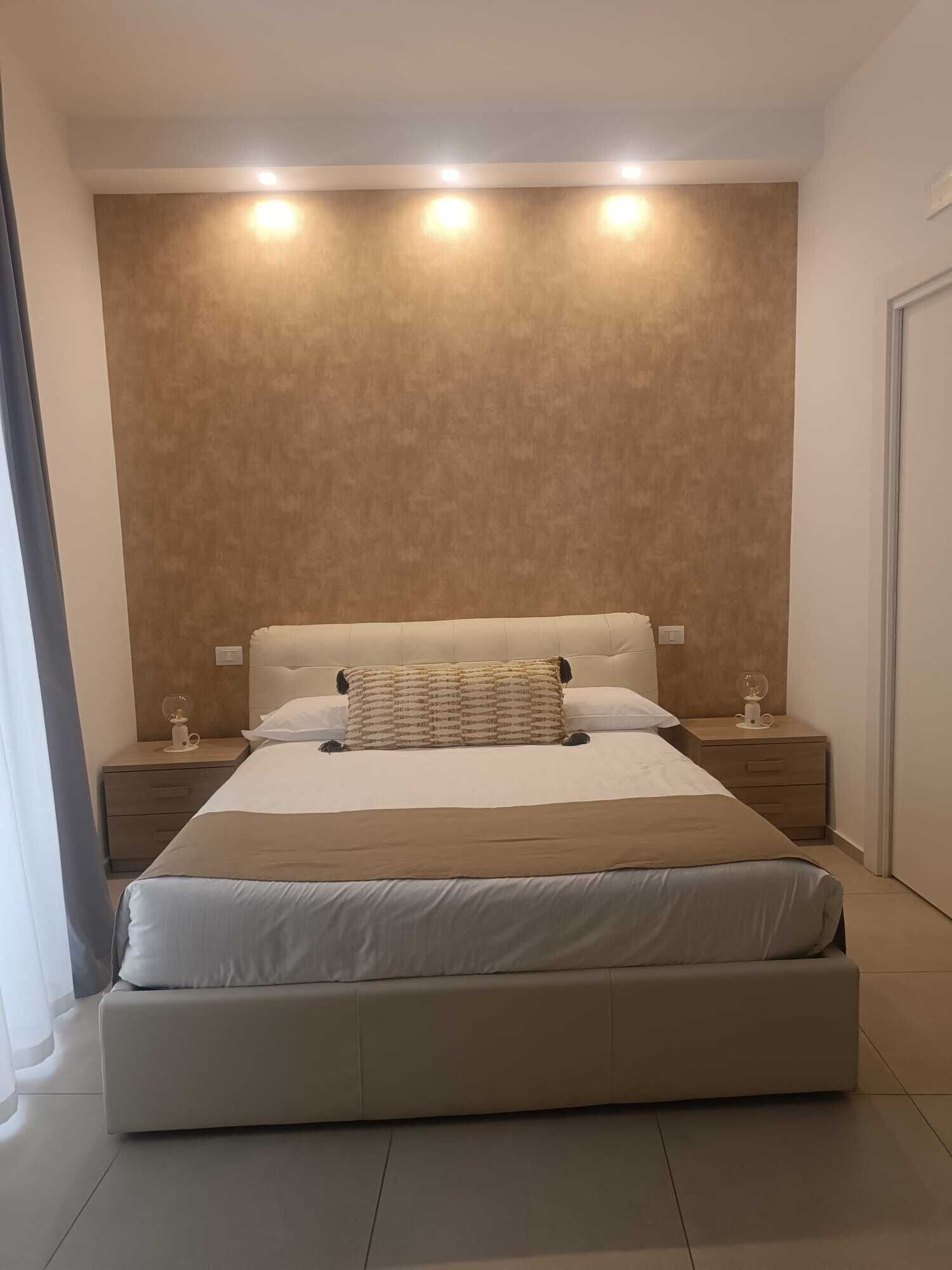 A modern bedroom with a large bed, two bedside tables, and a wall-mounted light fixture.