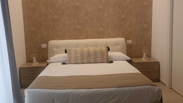 A modern bedroom with a large bed, two bedside tables, and a wall-mounted light fixture.