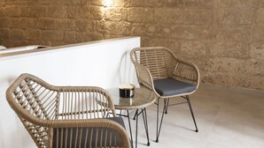 A room with a stone wall, two wicker chairs with cushions, a small round table, and a white counter. - Torre Canina Suite & Rooms  (Trani)