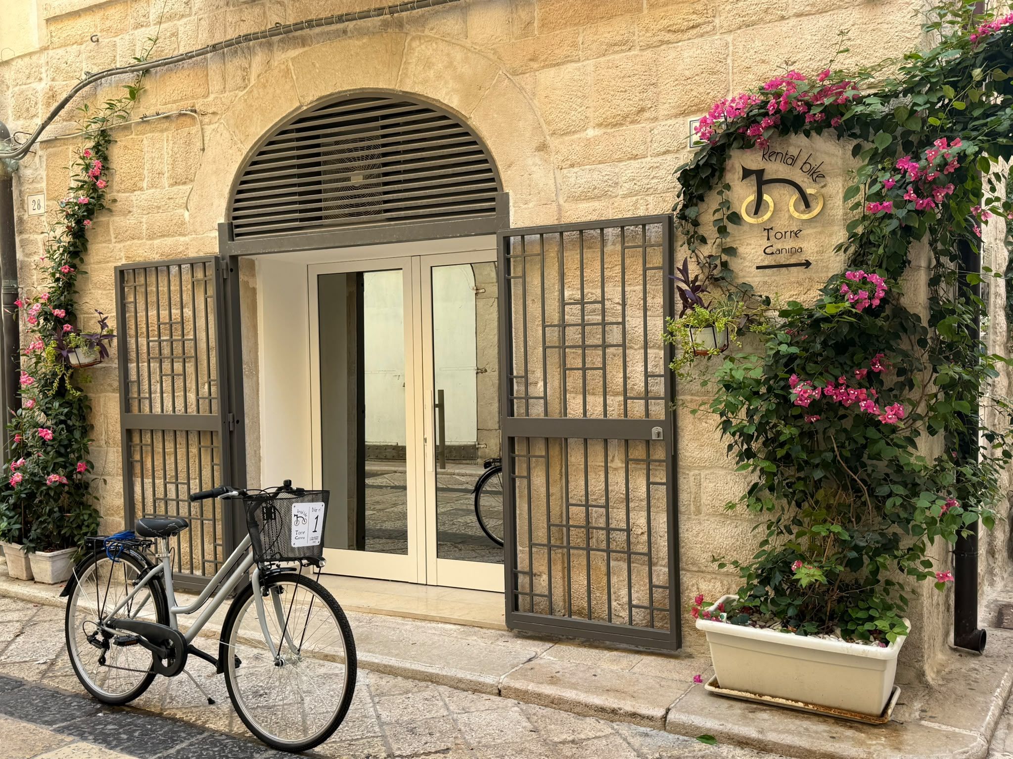 Un edificio con fachada de piedra, entrada protegida por una reja y una bicicleta estacionada afuera.