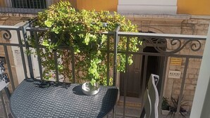 A balcony with a metal table and chairs, a potted plant, and a building with yellow walls and green shutters in the background. - Torre Canina Suite & Rooms  (Trani)