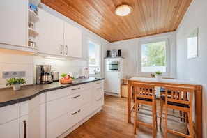 Una cocina moderna con armarios blancos, techo de madera y un comedor con dos sillas de madera.