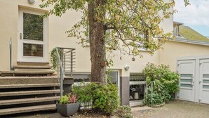 En bostadsbyggnad med en trappa som leder till entrén, ett stort träd och en garageport.