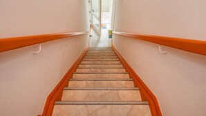 En trappa med orangea ledstänger och ett marmorgolv som leder till ett ljust område med en dörr och en färgglad matta.