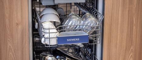 An open dishwasher with various dishes and utensils inside, and a Siemens label on the door.