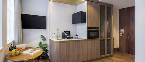A compact kitchen with a built-in microwave, a sink, and a coffee maker. There is a small dining area with a table and chairs, and a potted plant.