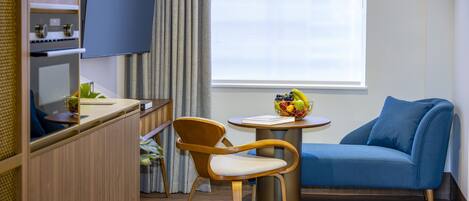A modern room with a blue sofa, wooden chair, and a small round table with a fruit bowl.