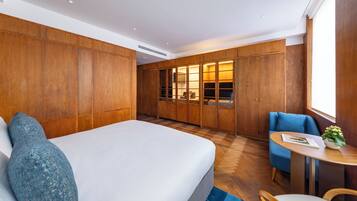 A modern hotel room with a large bed, wooden wardrobe, a small table with a plant, and a blue chair.