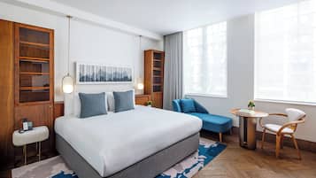 A modern hotel room with a large bed, a desk, a chair, and a small table.