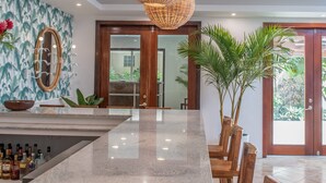 A modern kitchen with a marble countertop, wooden chairs, and a large woven light fixture.