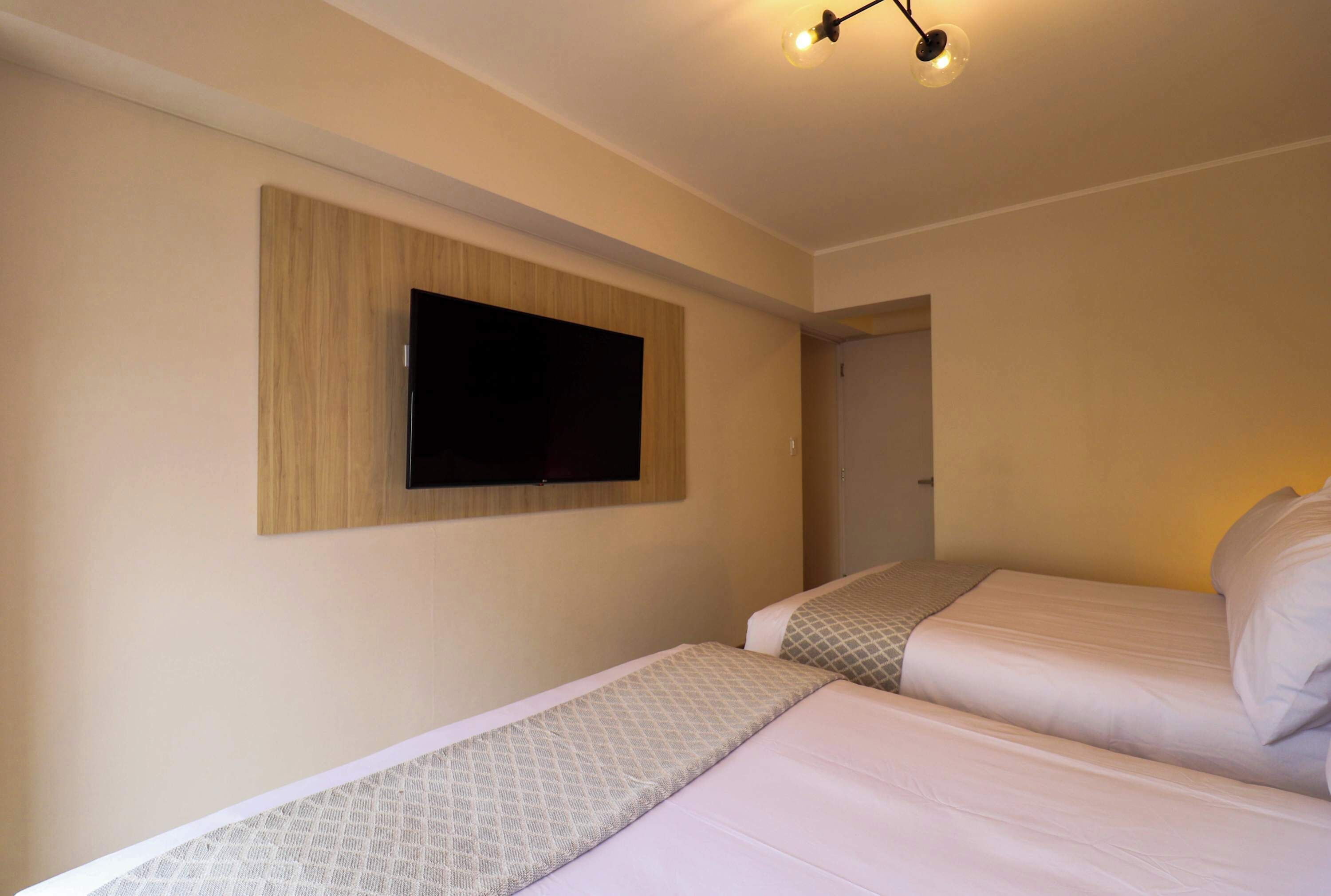A hotel room with two beds, a mounted TV, and a ceiling light fixture.
