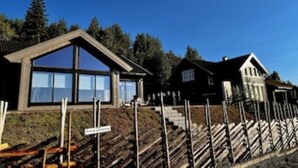 Een modern huis met grote ramen, een schuin dak en een houten omheining.