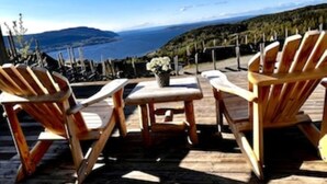 Een houten terras met twee Adirondack-stoelen en een kleine tafel, met uitzicht op een waterpartij en heuvels.