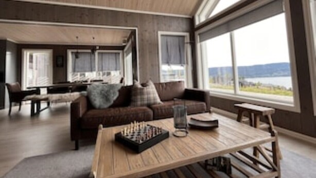 Een moderne woonkamer met een houten plafond, grote ramen, een bank, een salontafel en een schaakbord.