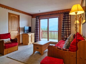 A cozy room with a wooden sofa, a television on a cabinet, and a view of the outdoors through a sliding glass door.