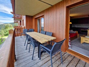 A wooden deck with a table and chairs, a balcony with a view of the mountains, and a room with a fireplace.