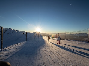 Pista de esqui coberta de neve, com esquiadores e um céu ensolarado.