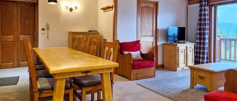 Een houten eettafel met stoelen, een bank, een televisie en een houten kast in een ruimte met een houten plafond en wanden.