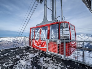 A red cable car with a triangular logo, suspended by cables, overlooking a snowy mountain landscape.