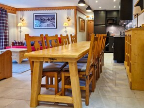 A dining area with a wooden table and chairs, a kitchen in the background, and a framed picture on the wall.
