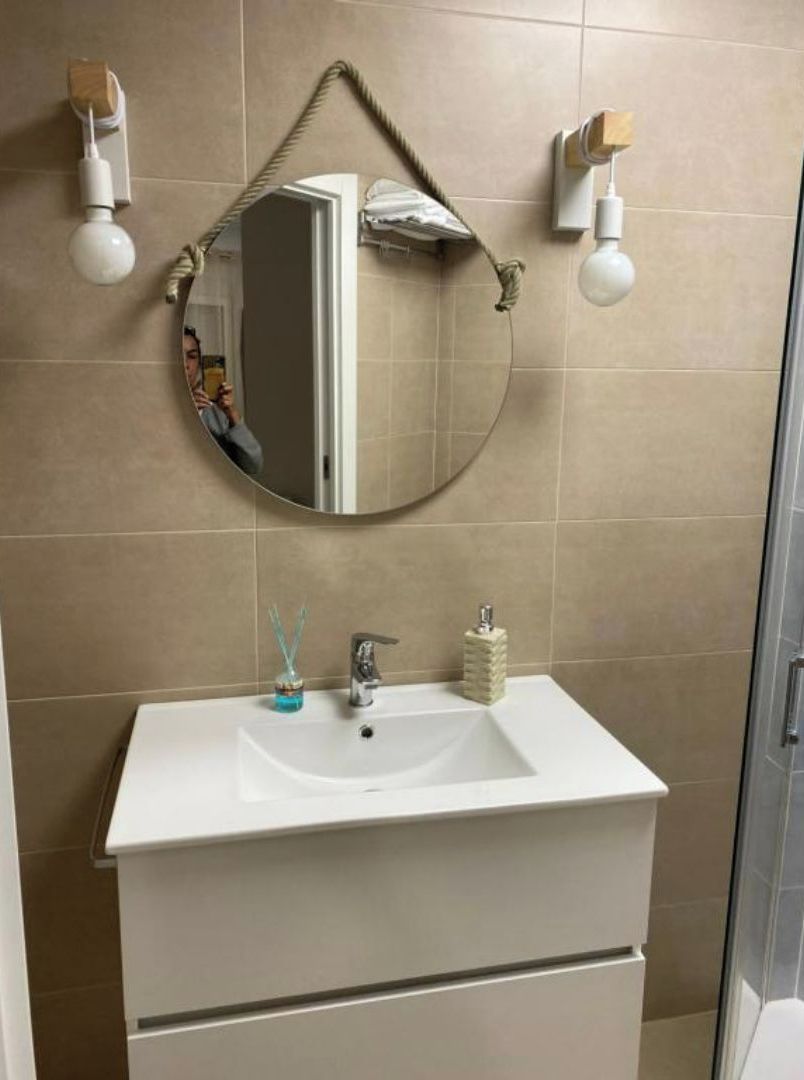 Un baño con un lavamanos blanco, un espejo redondo y dos luces fijadas a la pared.