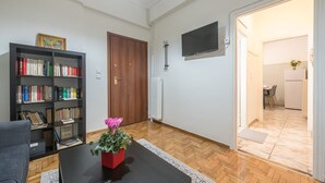 A living room with a bookshelf, a potted plant, a black coffee table, and a wooden floor. - Athens Apartment 5-min to Metaxourgeio Metro  (Athina)