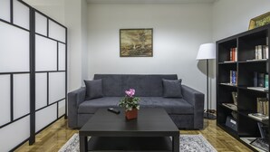 A living room with a grey sofa, a black coffee table with a flower vase, a bookshelf, and a painting on the wall. - Athens Apartment 5-min to Metaxourgeio Metro  (Athina)