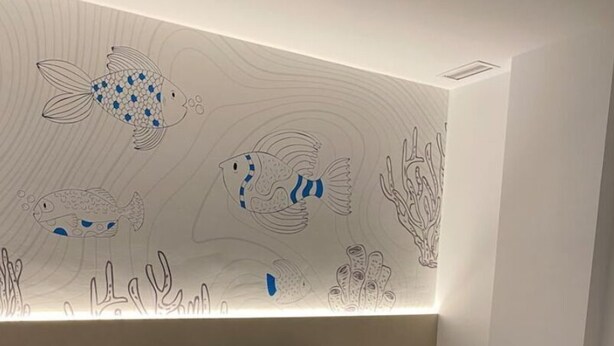 Ein modernes Schlafzimmer mit einem Bett, zwei Kissen, einem Nachttisch und einer Wandmalerei von Fischen und Korallen.