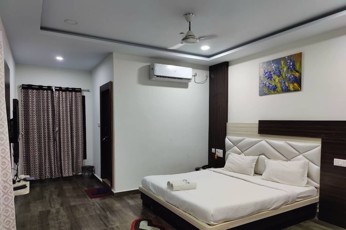 A hotel room with a bed, an air conditioning unit, a ceiling fan, a painting, and a heart-shaped rug on the floor.