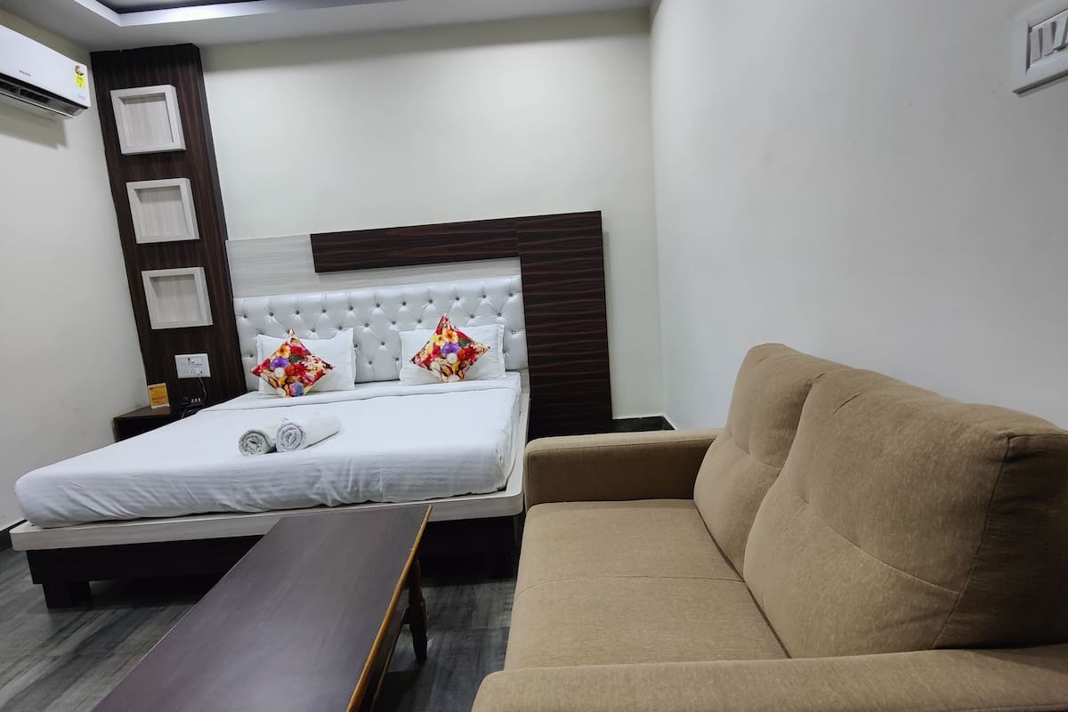 A modern hotel room with a bed, a sofa, a bench, and a ceiling fan.