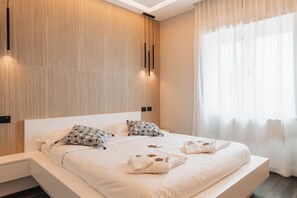Een moderne slaapkamer met een groot bed, twee kussens, een nachtkastje en een raam met dunne gordijnen.