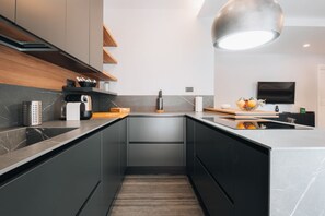 A modern kitchen with dark cabinetry, a marble countertop, and a built-in oven. - Sama Apartments – Elegance, Comfort and Sea View in the Heart of Sorrento (Sorrento)