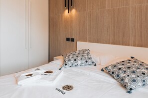Une chambre à coucher moderne avec une tête de lit en bois, un lit agrémenté d’oreillers à motifs et un lit parfaitement fait avec des serviettes.