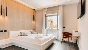 A modern bedroom with a large bed, a seating area, a window with a view, and a flat-screen TV mounted on the wall. - Sama Apartments – Elegance, Comfort and Sea View in the Heart of Sorrento (Sorrento)