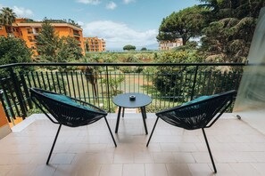 Un balcon avec deux chaises et une petite table, donnant sur un jardin et des immeubles.